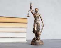 themis goddess of justice statuette on background of books on desktop. symbol of law with scales and sword in his hands. legal company or university of law and judicial structure. library education